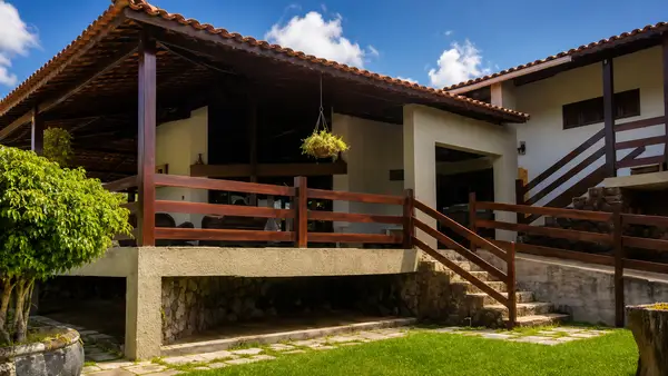 Fachada acolhedora da Clínica Recanto da Fazenda com varanda de madeira, jardim verde e escadaria de pedra