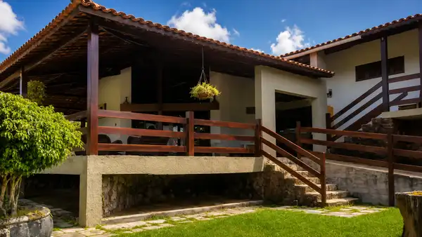 Fachada acolhedora da Clínica Recanto da Fazenda com varanda de madeira, jardim verde e escadaria de pedra