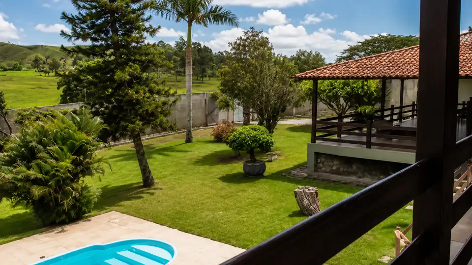 Vista da varanda da clínica com jardim exuberante, piscina e colinas ao fundo, transmitindo tranquilidade e conexão com a natureza